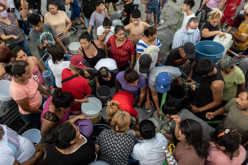El hombre con una gorra azul de béisbol llena las cubetas con agua de una pipa del gobierno.